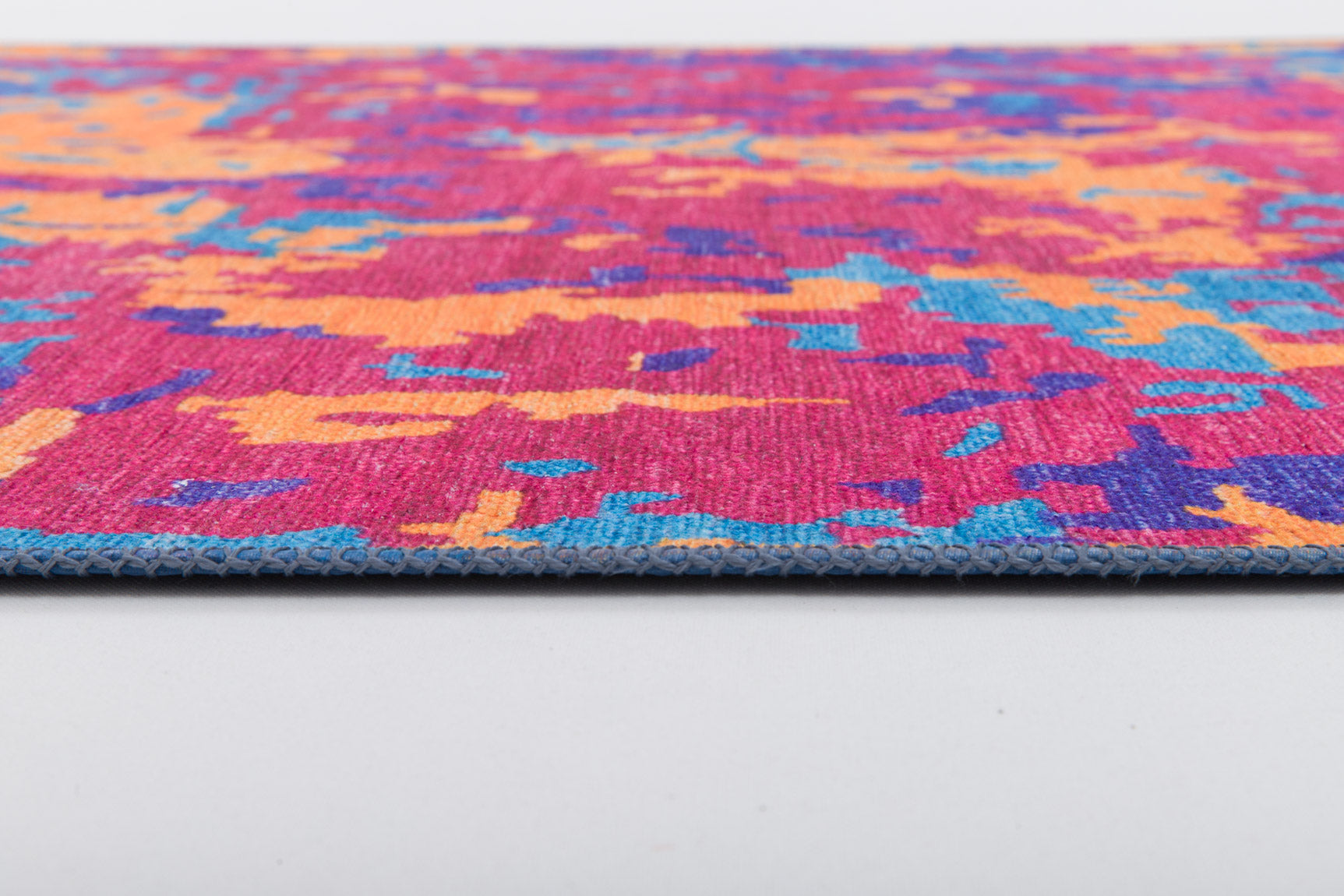 A close-up of the Celestial Tapestry - Washable Rug - JRS004 shows its colorful abstract pattern in pink, orange, blue, and purple on white. The visible edge reveals its thickness—perfect for high-traffic areas.