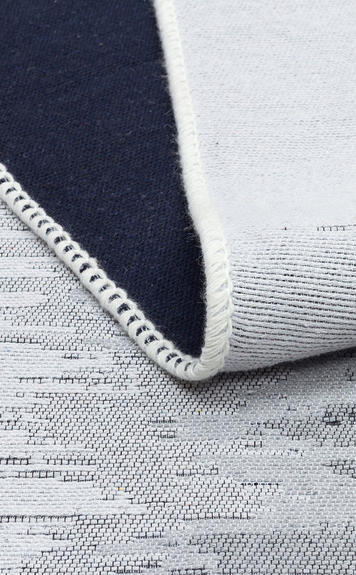 Load image 1 in gallery view. A close-up of the Charcoal Frame - Washable Double-Sided Kilims - AR40 shows a folded textile with one dark blue side, the other light gray with a subtle pattern, and an edge finished in white stitching.