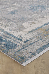 A close-up of the ChromaBurst Premium Rug - Blue - MT176, a machine-made rug with a distressed abstract pattern in blue, gray, beige, and white on a light wood floor. It features a visible woven edge and textured appearance.