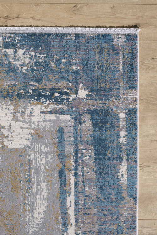 Load image 1 in gallery view. A close-up of the ChromaBurst Premium Rug - Blue - MT176, featuring abstract blue, gray, and beige patterns on light wooden flooring. The machine-made acrylic-viscose rug’s white fringe is visible along the top edge.