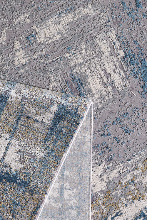 Load image 1 in gallery view. A close-up shows the ChromaBurst Premium Rug - Blue - MT176 folded over, highlighting its textured blue, gray, beige, and white surface with a subtle geometric and abstract motif.