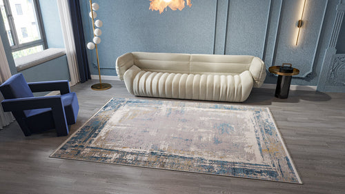 Load image 1 in gallery view. A modern living room with a beige curved sofa, blue armchair, floor lamp with round lights, round side table, and the ChromaBurst Premium Rug - Blue - MT176 on gray wood flooring. Light blue textured walls and a large window complete the space.