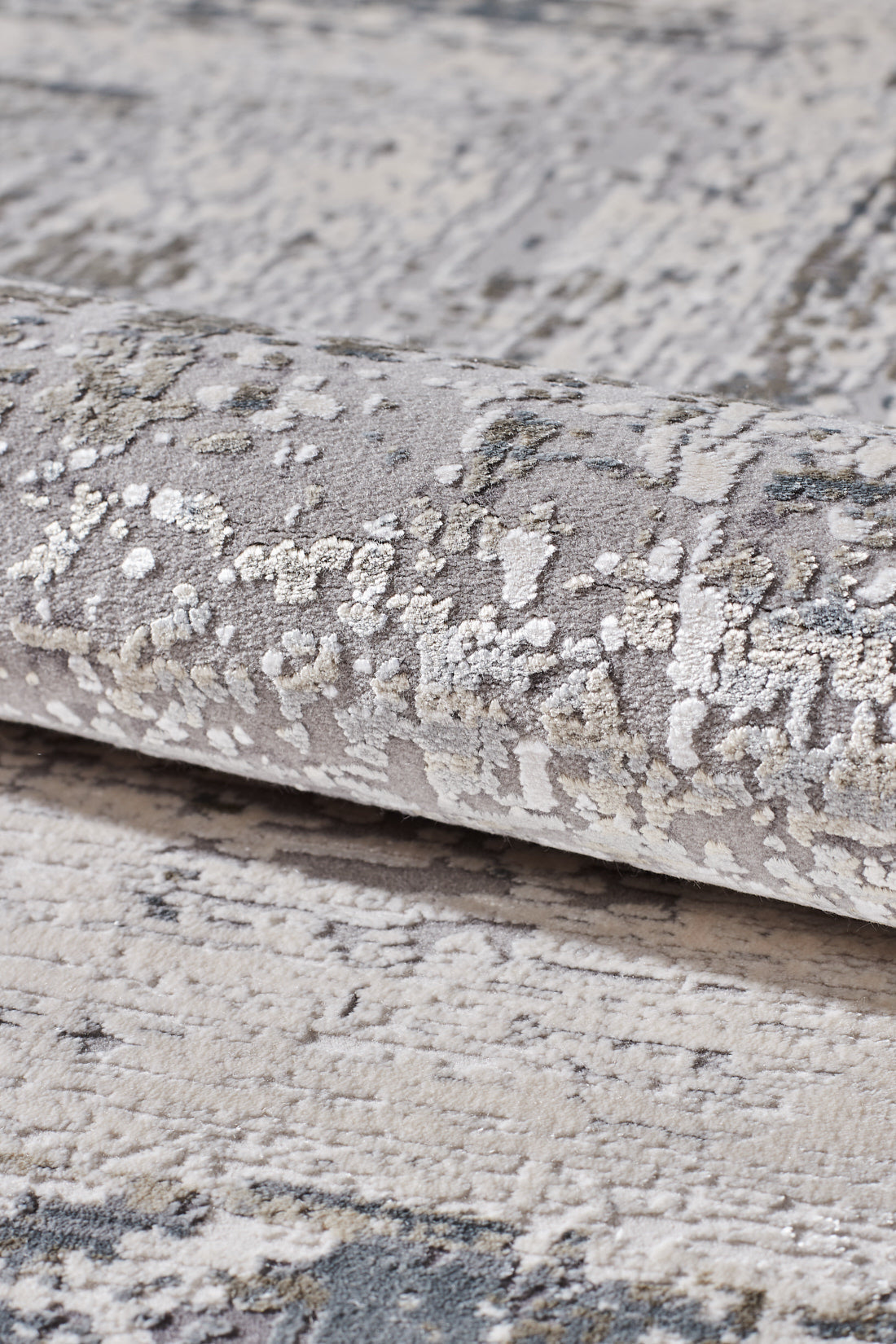 A close-up of the ChromaBurst Premium Rug - Bright - MT177 shows its rolled, textured surface with a plush, abstract mottled design in gray, off-white, and beige tones—perfect for adding a modern touch to your space.