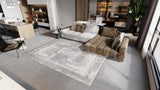 Modern living room with a gray sectional, brown chaise, ChromaBurst Premium Rug - Bright (MT177) featuring abstract patterns, large windows, an indoor plant, and an open kitchen with wooden accents. Neutral tones and contemporary decor.