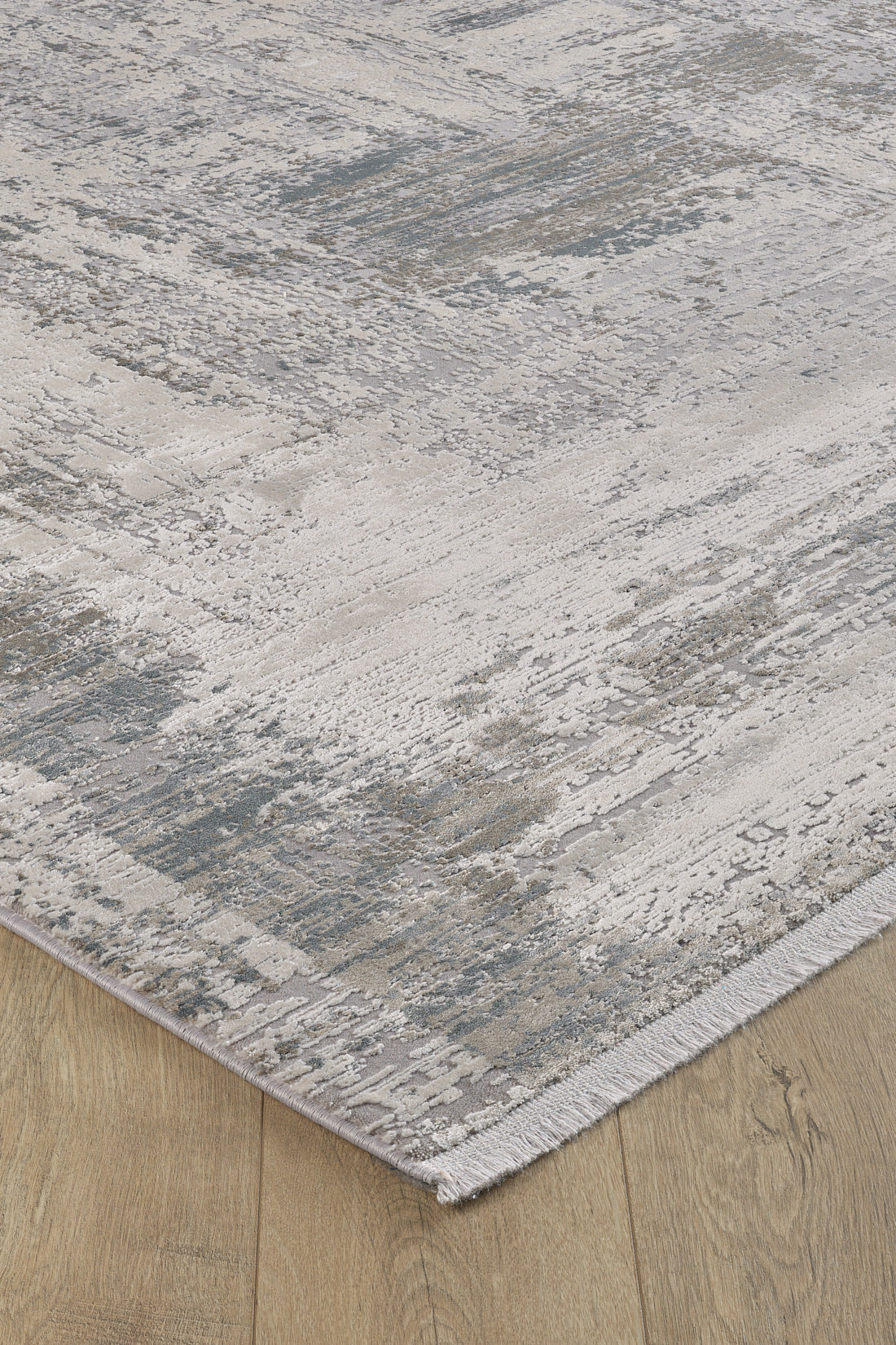 A close-up of the ChromaBurst Premium Rug - Bright - MT177, a machine-made acrylic-viscose rug with an abstract gray, cream, and blue pattern, textured surface, short fringe, and shown on a light wood floor.