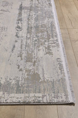 A close-up of the ChromaBurst Premium Rug - Bright - MT177, a modern acrylic-viscose piece with a textured abstract gray and beige design, thin light border, and visible fringes, displayed on a light wood floor.