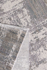 A close-up of the ChromaBurst Premium Rug - Bright - MT177 shows its abstract gray, cream, and beige pattern. One corner is folded over, revealing the stylish machine-made edges and underside.