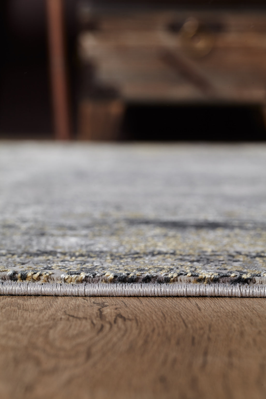 Close-up of the ChromaBurst Premium Rug - Dark - MT175 in gray and yellow on a wooden floor, with soft-focus furniture in the background.