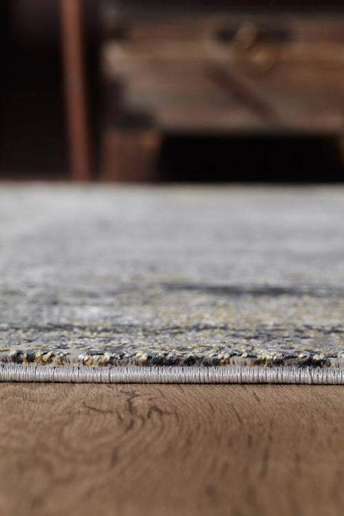 Load image 1 in gallery view. Close-up of the ChromaBurst Premium Rug - Dark - MT175 in gray and yellow on a wooden floor, with soft-focus furniture in the background.
