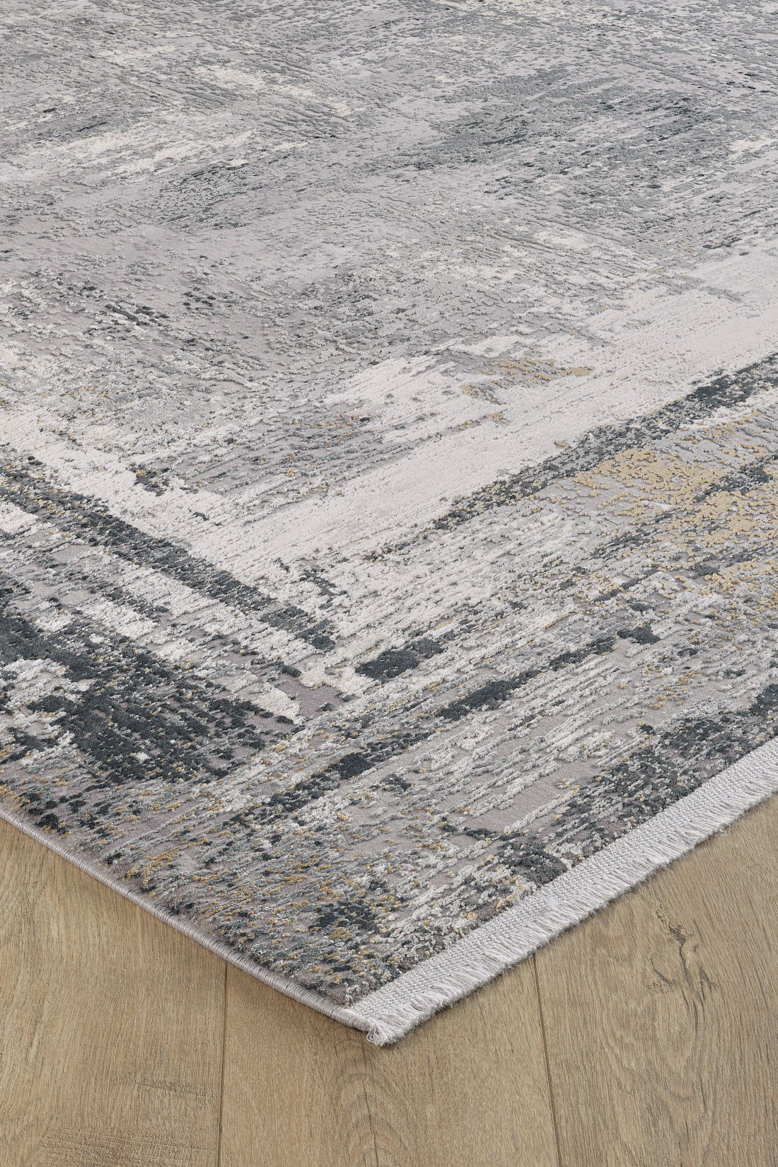 Close-up of the ChromaBurst Premium Rug - Dark - MT175, featuring an abstract gray, white, and beige pattern with short fringe on the edge, lying on a light wood floor. This modern rug is machine-made.