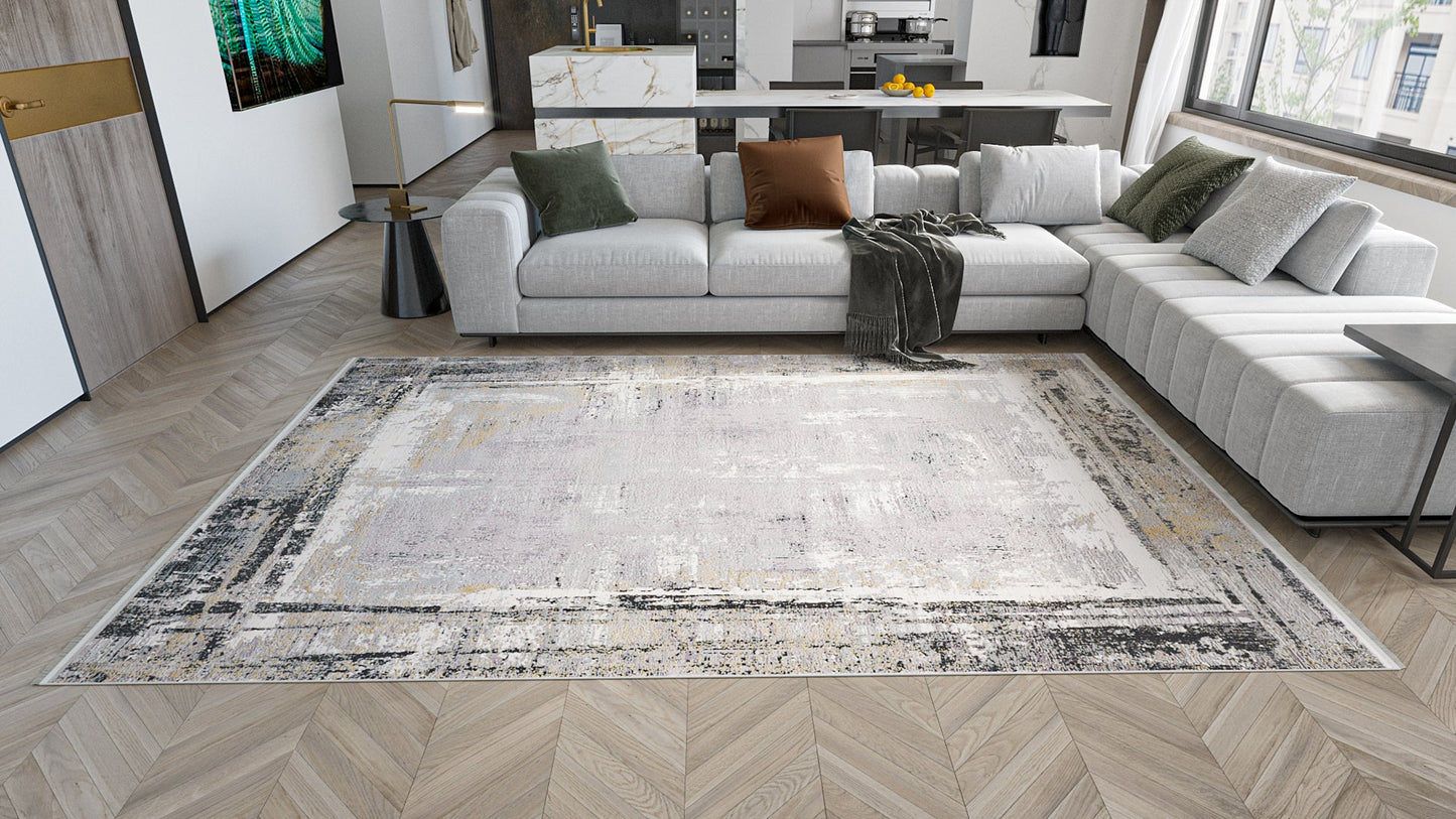 A modern living room with a light gray sectional sofa, assorted throw pillows, a dark throw blanket, wood herringbone flooring, an open kitchen in the background, and a large ChromaBurst Premium Rug - Dark - MT175.