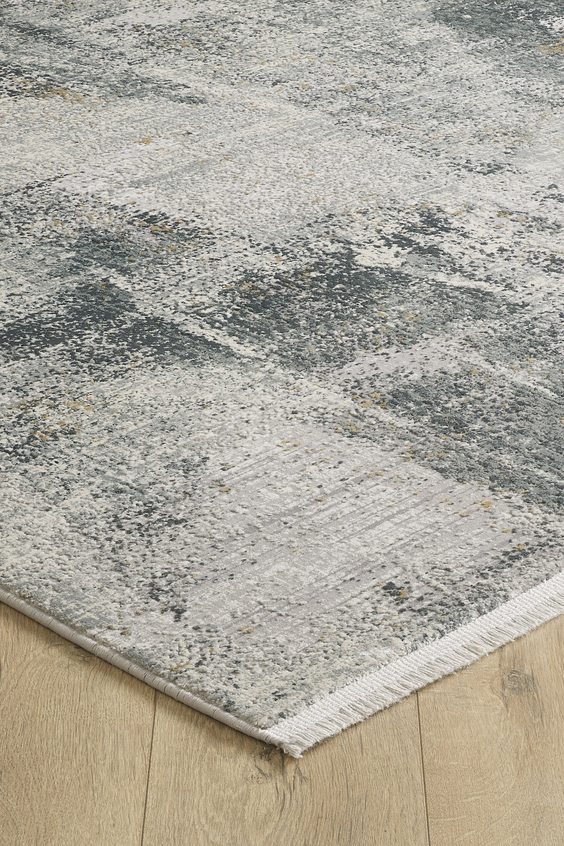 A close-up of the Chromatic Flair Contemporary Rug - Charcoal - M660A, showing its abstract gray, white, and blue pattern with textured surface and fringe, placed on a light wood floor.