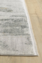 A close-up of the Chromatic Flair Contemporary Rug - Charcoal - M660A, a modern machine-made rug with subtle abstract patterns and short fringe, shown on a light wood floor.