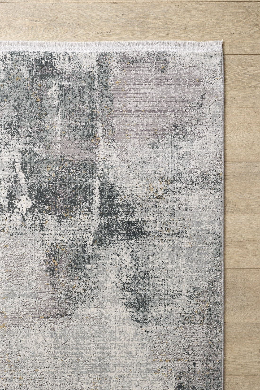 The Chromatic Flair Contemporary Rug - Charcoal (M660A) is a modern, machine-made rug with a distressed grey, white, and light purple design and a stylish fringed edge, shown partially on a light wooden floor.