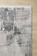 The Chromatic Flair Contemporary Rug - Charcoal (M660A) is a modern, machine-made rug with a distressed grey, white, and light purple design and a stylish fringed edge, shown partially on a light wooden floor.