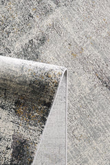 A close-up of the Chromatic Flair Contemporary Rug - Charcoal (M660A) shows its abstract, textured pattern in gray, cream, and gold hues with a soft woven look and a folded corner.