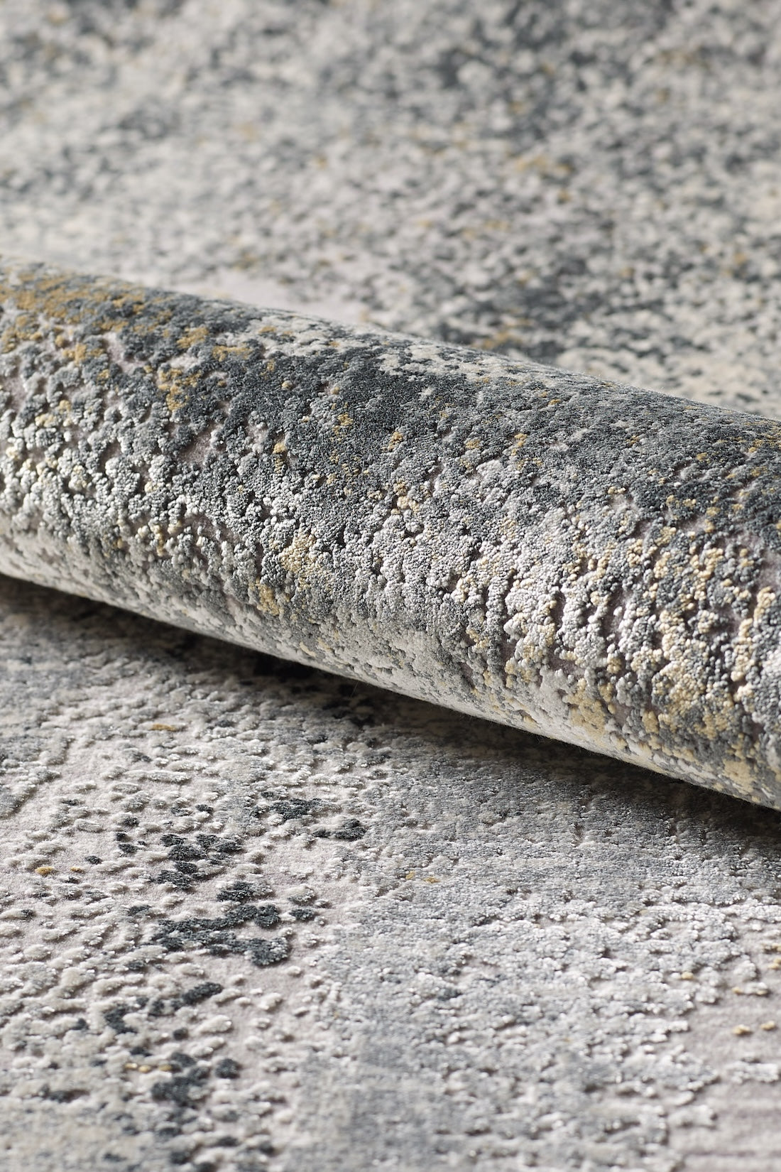 A close-up of the Chromatic Flair Contemporary Rug - Charcoal (M660A) shows an abstract, textured pattern in gray, beige, and cream with distressed detailing and raised areas for a multidimensional look.