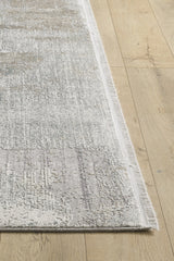 A close-up of the Chromatic Flair Contemporary Rug - Latte - M660D shows its textured light grey and beige surface with fringed edges, machine-made and placed on a light wooden floor, highlighting both the rug and part of the surrounding area.