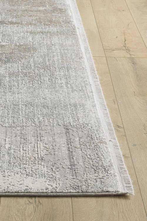 Load image 1 in gallery view. A close-up of the Chromatic Flair Contemporary Rug - Latte - M660D shows its textured light grey and beige surface with fringed edges, machine-made and placed on a light wooden floor, highlighting both the rug and part of the surrounding area.