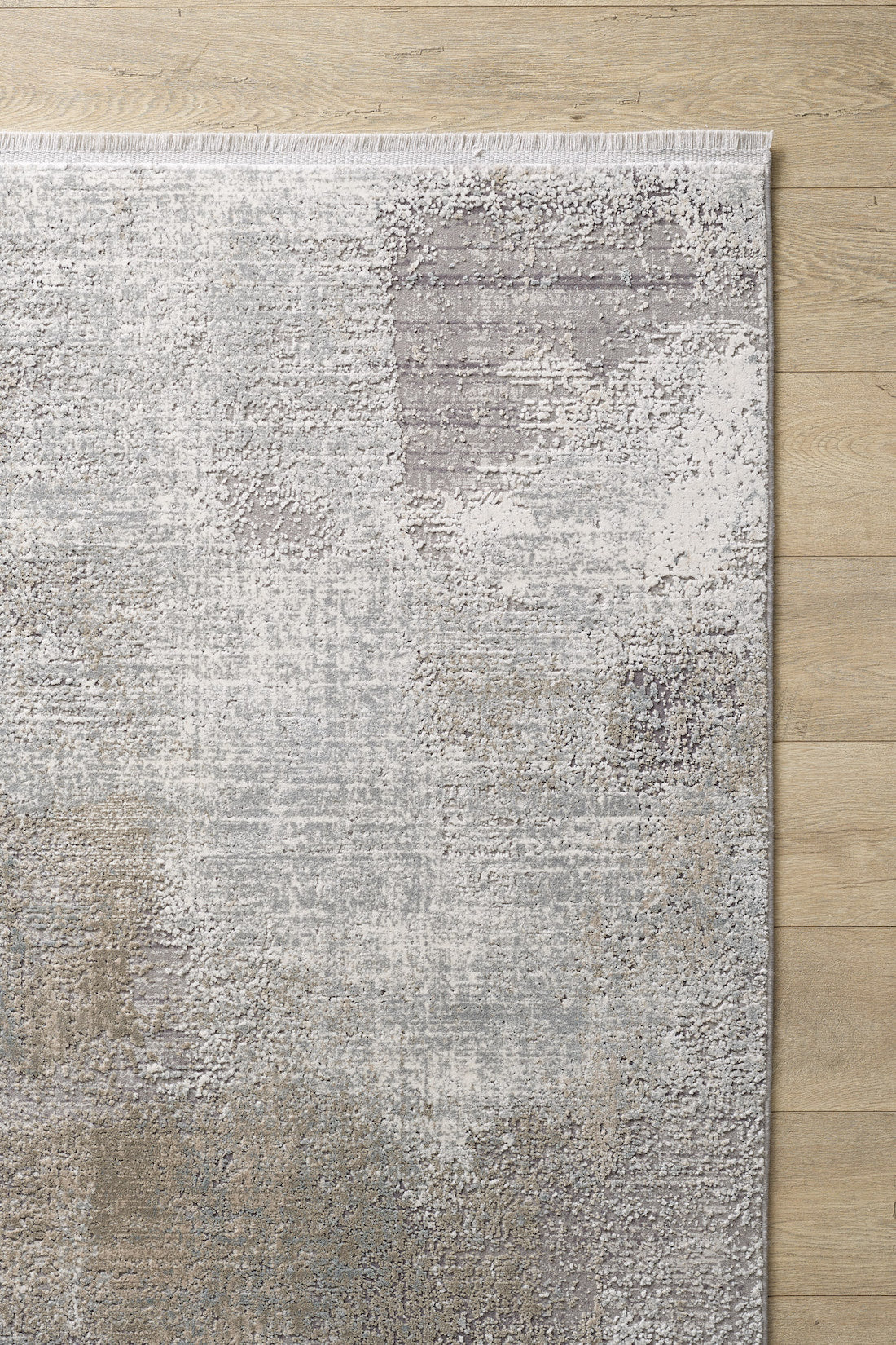 The Chromatic Flair Contemporary Rug - Latte - M660D, with its mottled gray, beige, and ivory pattern and fringed edge, brings abstract style and texture to any space atop a light wood floor.