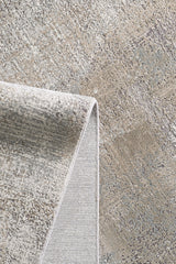 A close-up of the Chromatic Flair Contemporary Rug - Latte - M660D showcases its textured surface in gray, beige, and tan hues, with a folded corner revealing both the modern pattern and underside of this stylish machine-made rug.