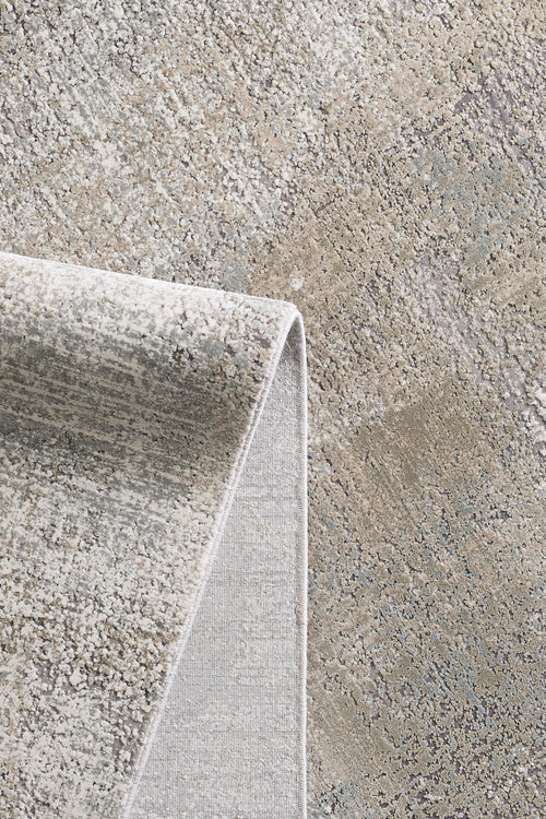 Load image 1 in gallery view. A close-up of the Chromatic Flair Contemporary Rug - Latte - M660D showcases its textured surface in gray, beige, and tan hues, with a folded corner revealing both the modern pattern and underside of this stylish machine-made rug.