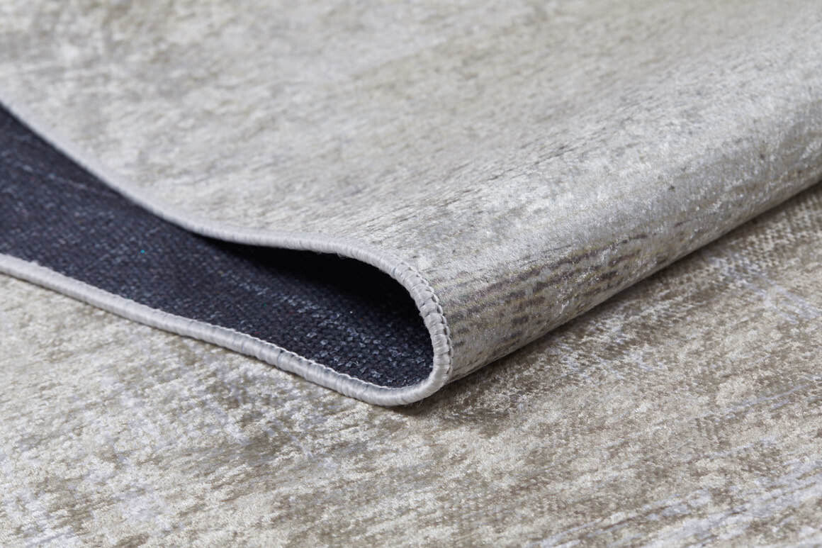 A close-up of the Cinnamon Swirl - Washable Rug - JR425 (Custom Size) shows its cream and beige flat weave, soft texture, subtle pattern, stitched edge, and lifted corner revealing the dark non-slip backing.