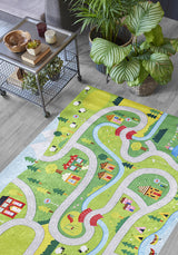 The City Adventure - Machine-Washable Rug JRC039 (Custom Size) adds color with winding roads, rivers, houses, trees, and animals—ideal for high-traffic areas—and is shown on a wooden floor beside a metal table with snacks and plants.