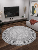 A modern living room features the Classic Contrast - Washable Rug - JR1985 on wooden flooring, a wall-mounted TV, a low decor shelf, a beige sofa with an orange throw, abstract wall art, and plants in the corners.