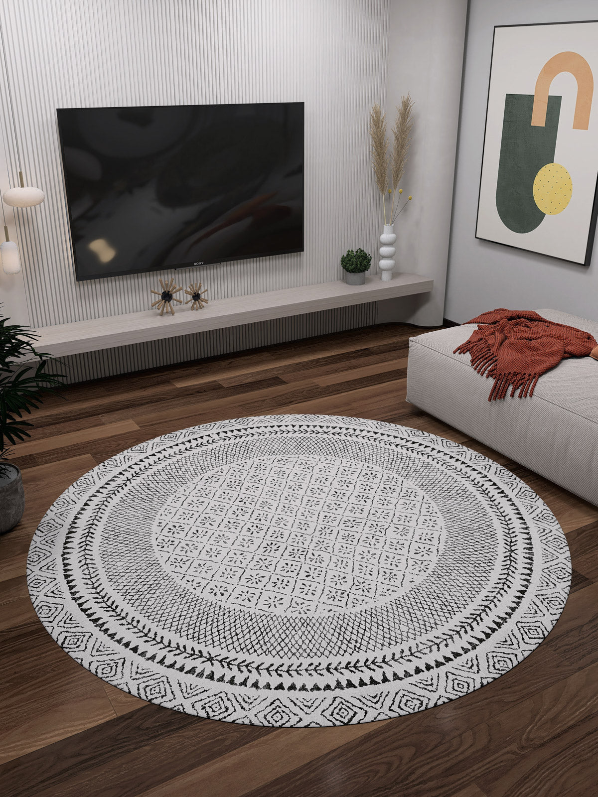 A modern living room with the Classic Contrast - Washable Rug - JR1985 (Custom Size) on wooden floors, a wall-mounted TV, minimalist shelves, potted plant, abstract art, and a sofa draped with an orange throw blanket.