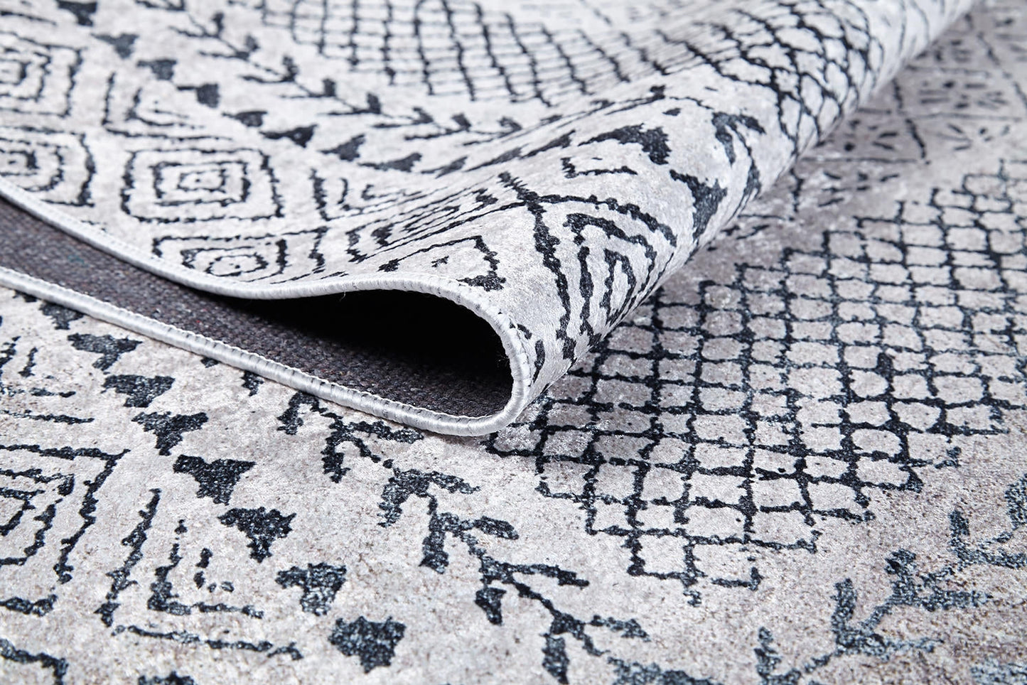 A close-up of the Classic Contrast - Washable Rug - JR1985 (Custom Size) in gray-anthracite, featuring a folded corner that highlights its flat weave texture and intricate geometric and floral patterns on both sides.