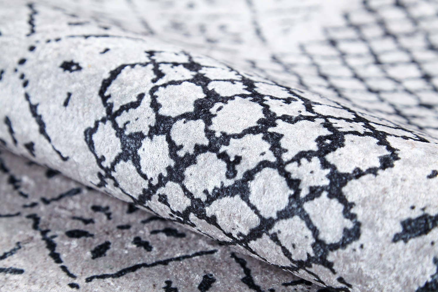 A close-up of the Classic Contrast - Washable Rug - JR1985 (Custom Size), rolled up to showcase its black geometric and abstract pattern on a light gray flat weave with soft texture and visible fibers.