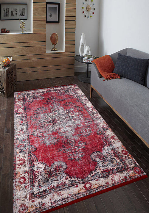 Load image 1 in gallery view. A modern living room with dark wood floors features the Classic Revival - Washable Rug - JR1374 (Custom Size) in red pattern, ideal for high-traffic areas, plus a gray sofa with orange and black cushions, a round side table, shelf, and wall clock.