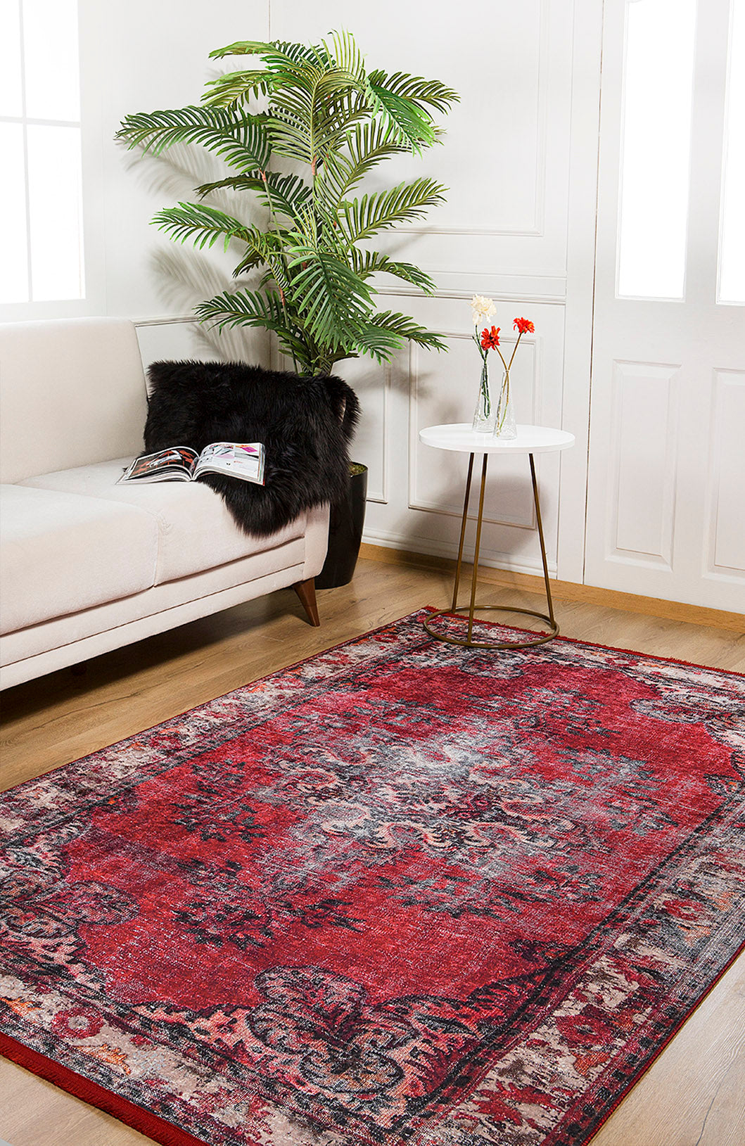 The Classic Revival - Washable Rug - JR1374 (Custom Size) adds vibrant red patterns to a bright room with wooden floors, white walls, and a white sofa—ideal for high-traffic areas and easy to keep clean.