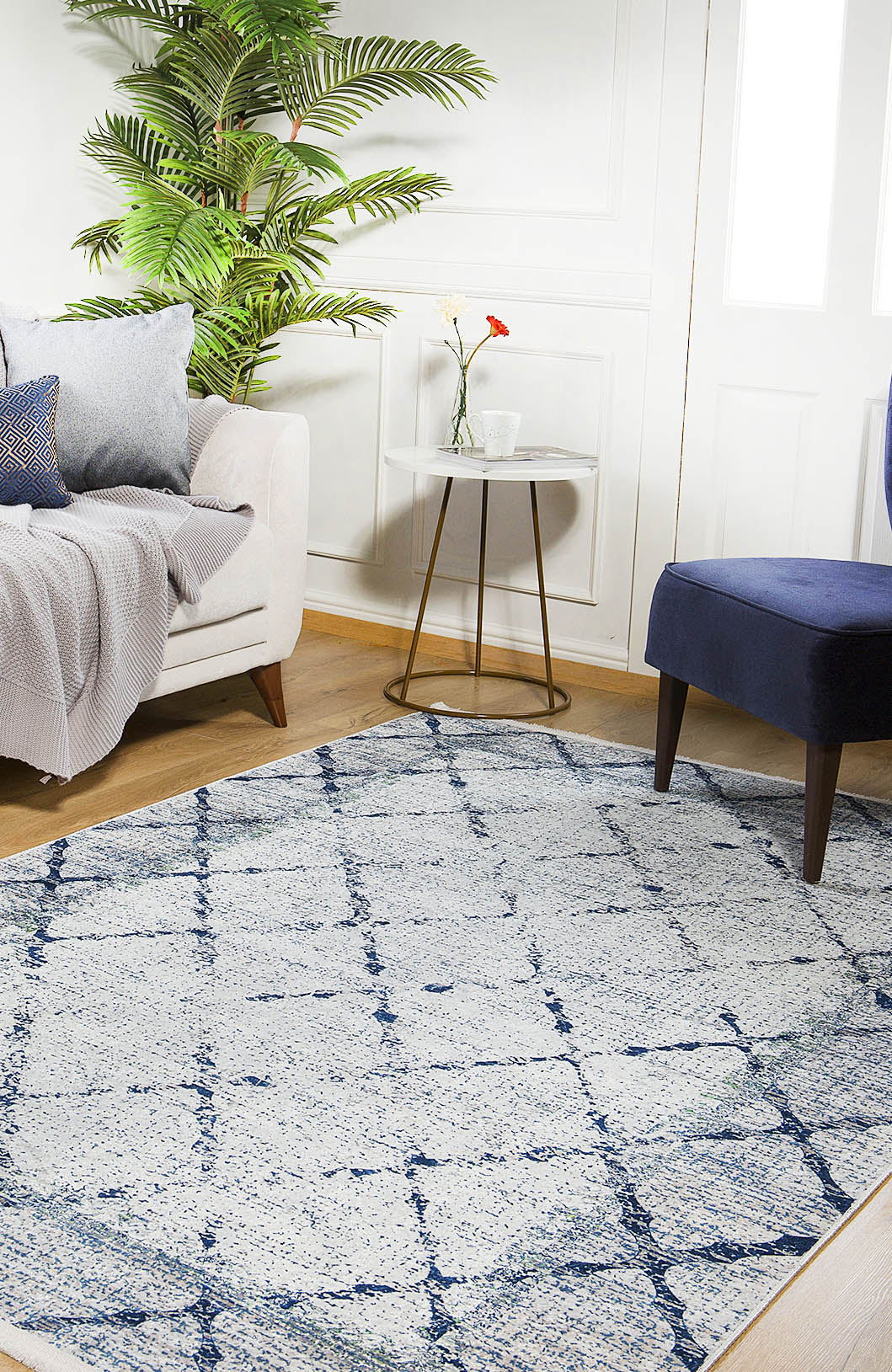 A cozy living room features a white sofa, blue chair, side table with a flower vase, potted plant, and the Classic Trellis - Washable Rug - JR710 on wooden floors. Natural light highlights the rug's stylish and allergy-friendly design.