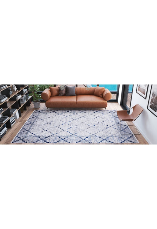 Load image 1 in gallery view. A modern living room with a tan leather sofa, brown accent chair, bookshelves, a potted plant, and the Classic Trellis - Washable Rug - JR710 (Custom Size), featuring blue geometric patterns on a wooden floor.