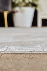 Close-up of the Cloudscape Geometry Modern Rug - M533B, light-toned and machine-made, on a wooden floor; a blurred white plant pot and part of a chair are visible in the background.