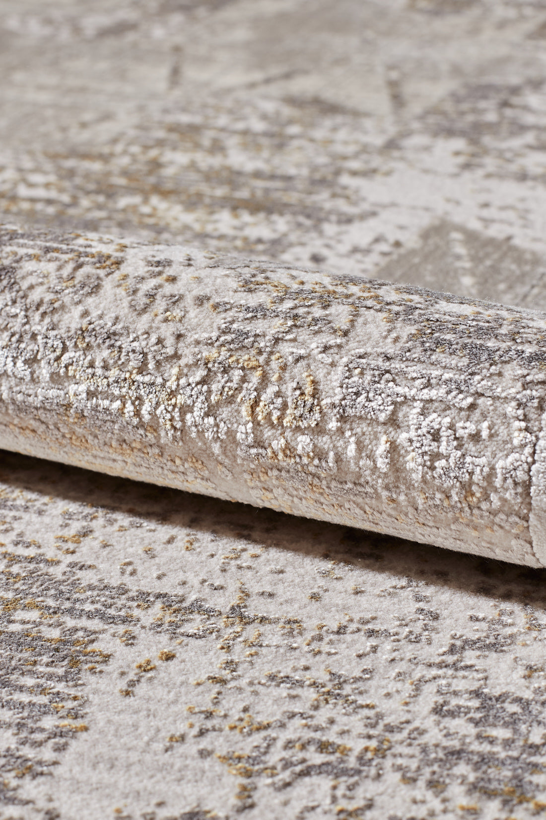 A close-up of the Cloudscape Geometry Modern Rug - M533B, a rolled-up beige and gray acrylic-viscose rug with an abstract pattern and subtle gold accents.