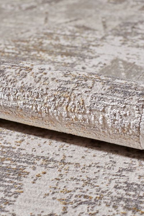 Load image 1 in gallery view. A close-up of the Cloudscape Geometry Modern Rug - M533B, a rolled-up beige and gray acrylic-viscose rug with an abstract pattern and subtle gold accents.