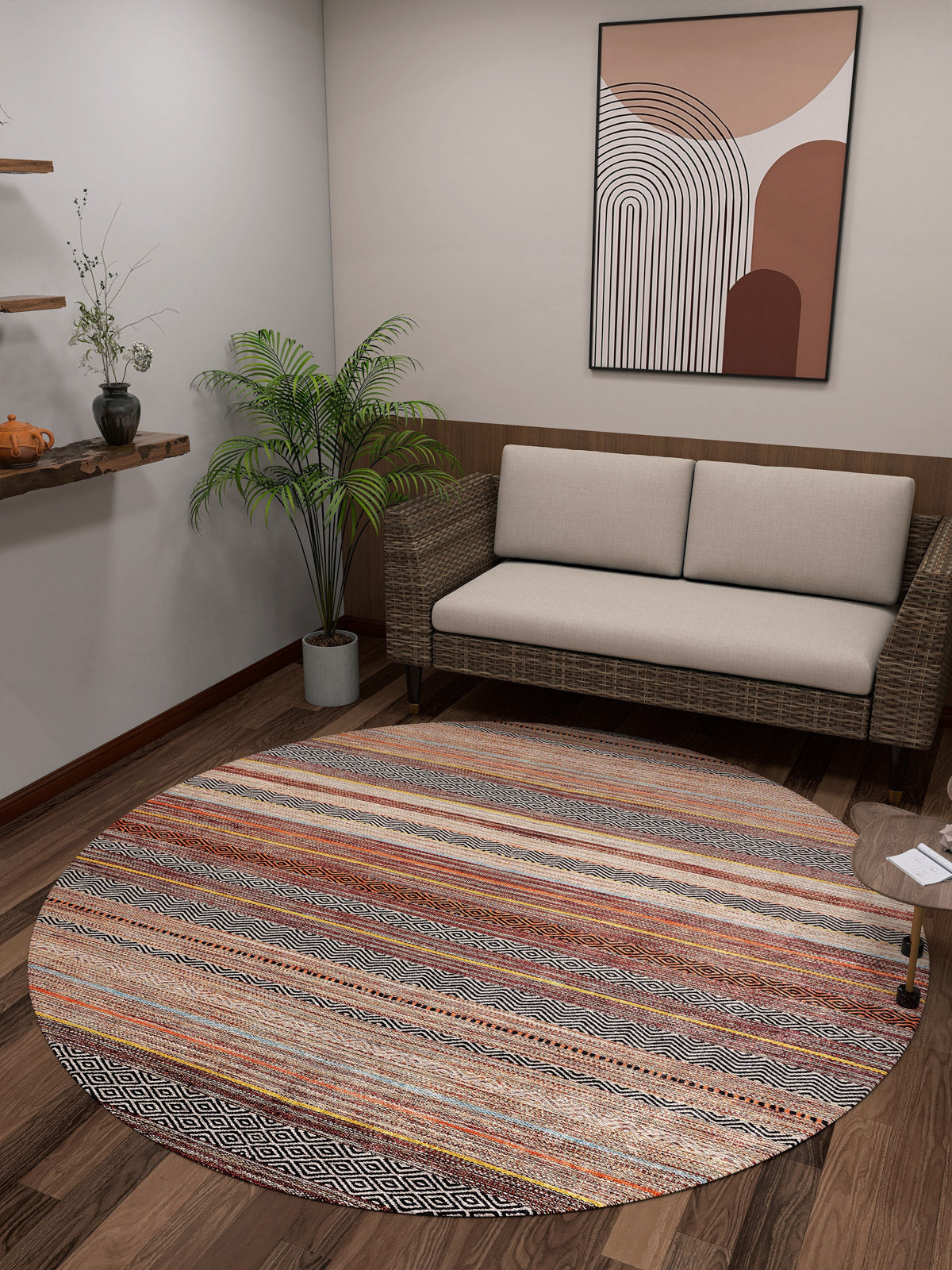 A cozy room featuring a beige wicker loveseat, potted plant, floating shelves with decor, wood flooring, abstract neutral wall art, and the allergy-friendly Coastal Breeze - Washable Rug - JR1549 in a multicolored round design.