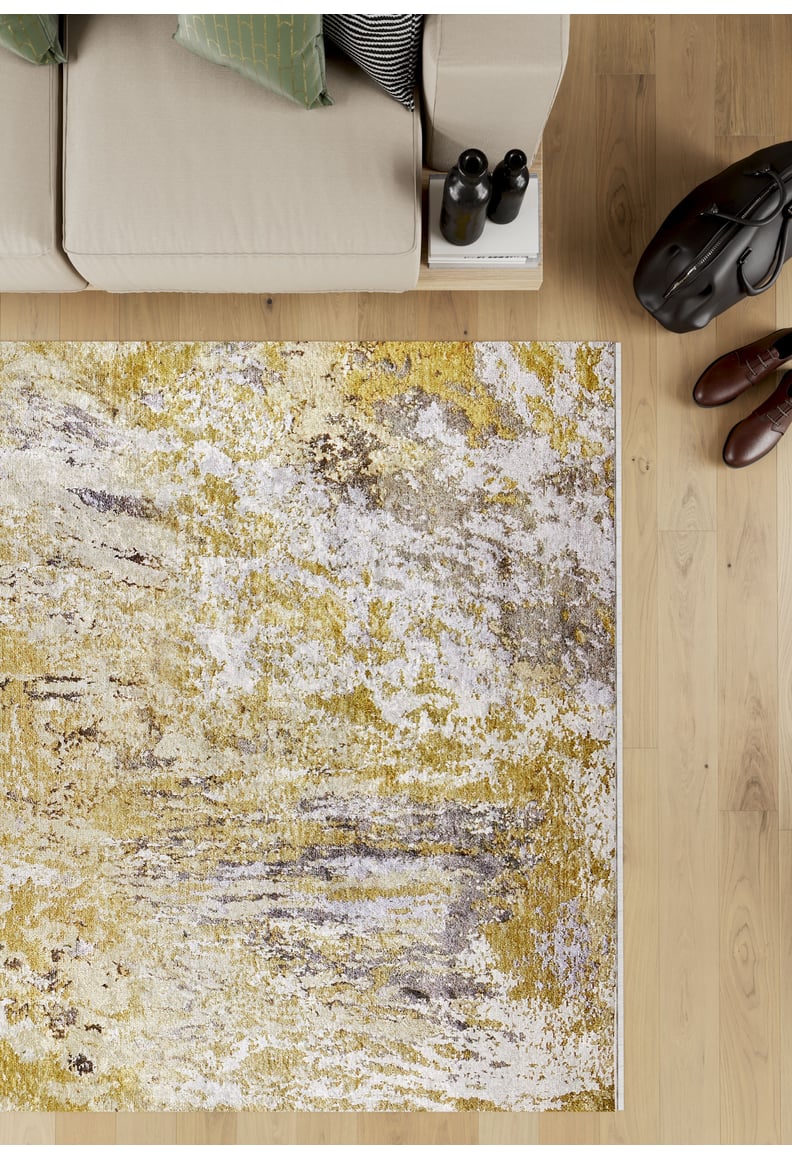 A modern living room with a beige sofa, patterned pillows, books, bottles, brown shoes, a black bag, and the Color Splash - Washable Rug - JR146 (Custom Size)—ideal for high-traffic areas—on a light wooden floor.