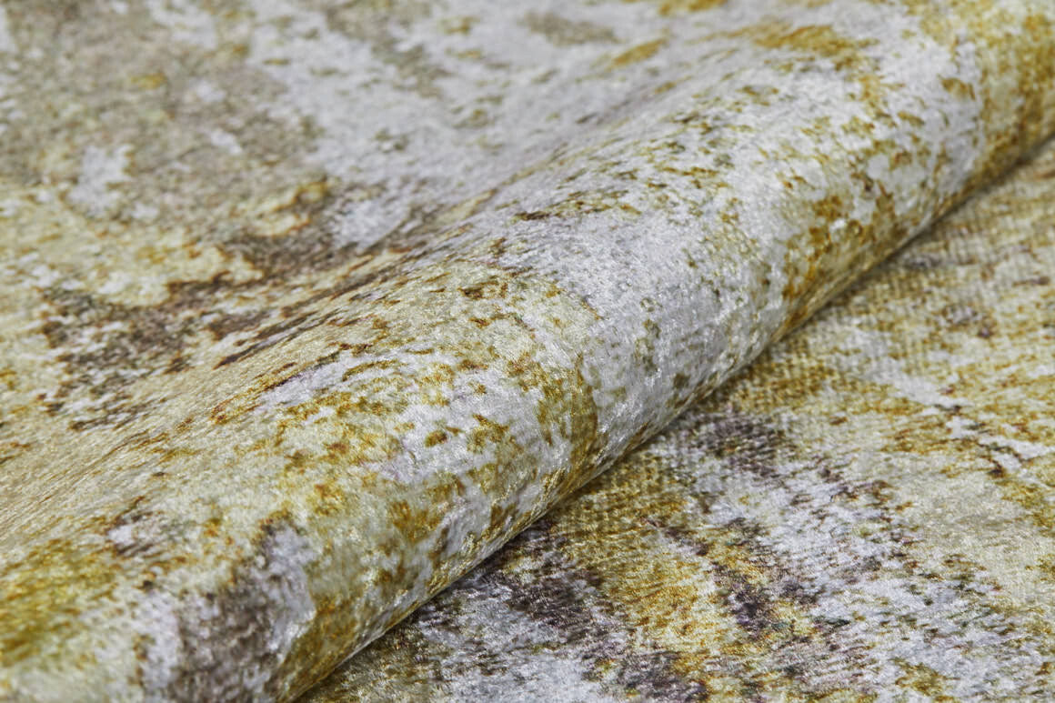 A close-up of the Color Splash - Washable Rug - JR146 (Custom Size), folded to show its washable, textured surface with a mottled abstract pattern in gold, beige, and gray tones.