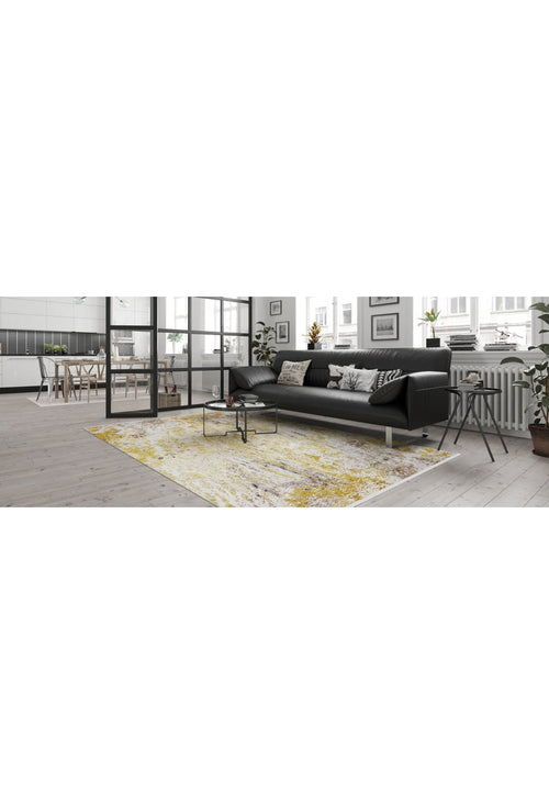Load image 1 in gallery view. A modern living room features the Color Splash - Washable Rug - JR146 (Custom Size) in yellow-gold, with a black sofa, patterned cushions, coffee table, large windows, and indoor plants. Bold color and style for chic everyday comfort.