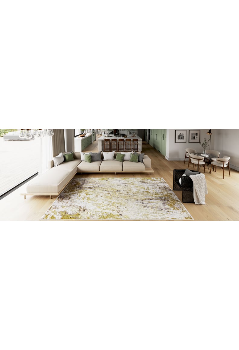 A modern open-plan living and dining area features a light sectional sofa, green and gray pillows, the Color Splash - Washable Rug - JR146 (Custom Size), a dining table with chairs, and large windows that fill the space with natural light.
