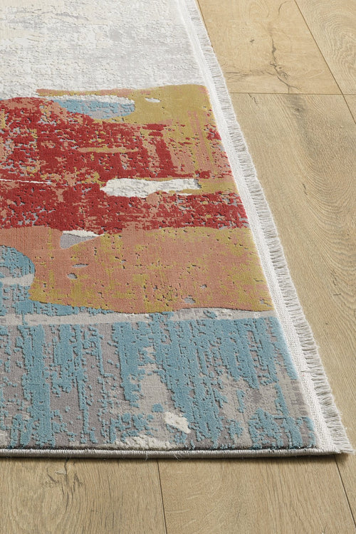 Load image 1 in gallery view. A close-up of the Colorful Chaos Premium Rug - M313P, showcasing its modern abstract patterns in red, gold, blue, and white with a white fringe, laid on a light wood floor.