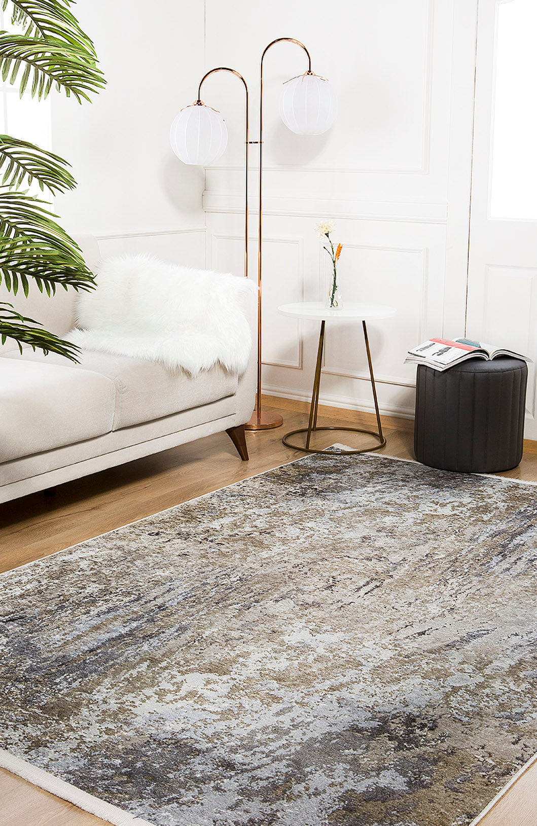 A modern living room features a light sofa, faux fur throw, round side table with vase and flower, ottoman, two-globe floor lamp, and the Contemporary Canvas - Washable Rug - JR145 (Custom Size) in yellow-gold on wooden flooring.