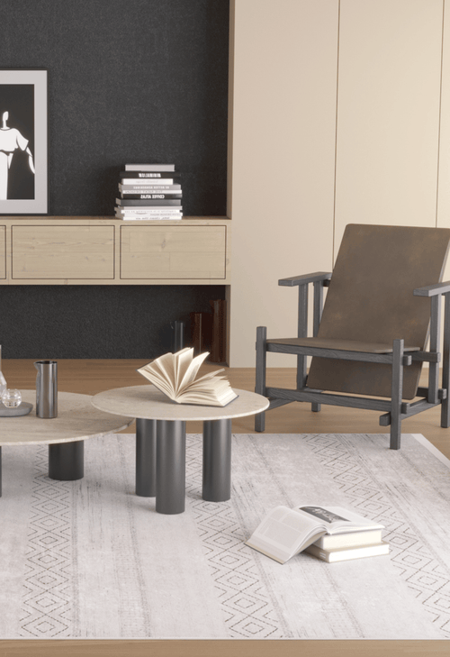 Load image 1 in gallery view. A modern living room features a wooden armchair, two round coffee tables, an open book on the Contemporary Coordinates - Washable Rug - JR750 (Custom Size)—ideal for high-traffic areas—a sideboard with books, and minimalist artwork on a dark wall.