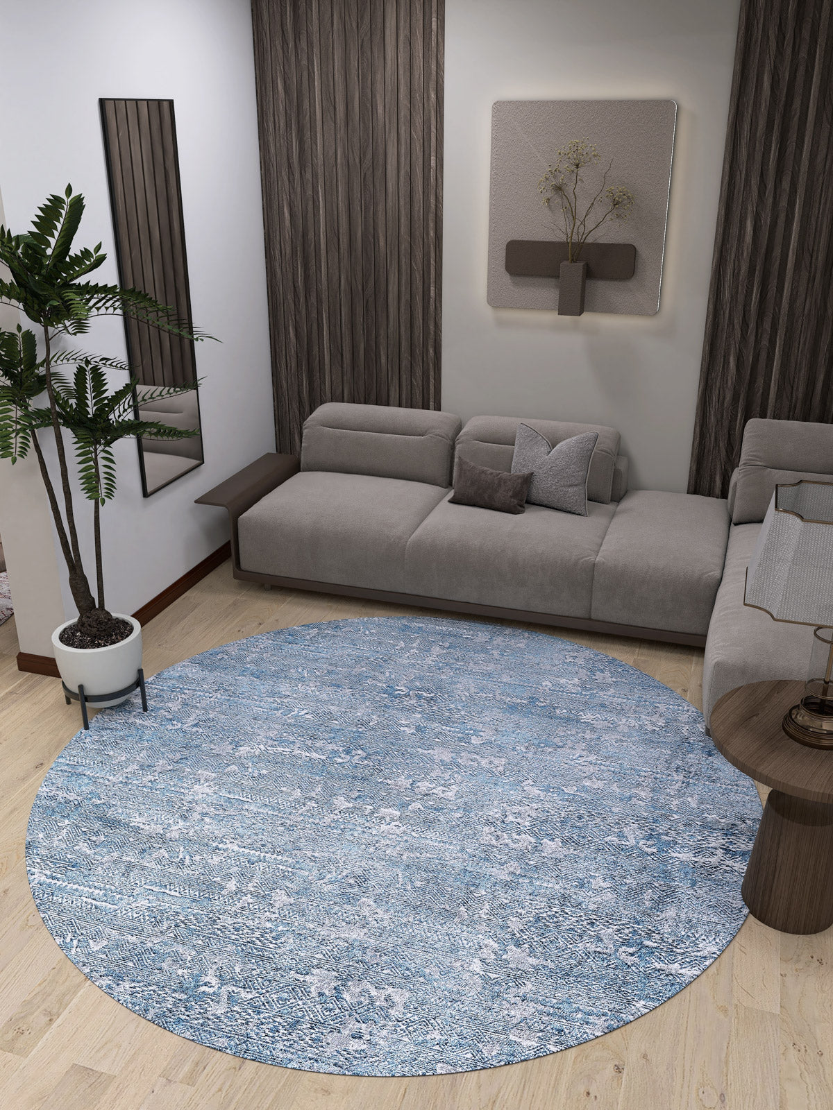 A modern living room with a gray sectional, wood-accented walls, wall art, a potted plant, and a small side table on light wood floors. The Contemporary Serenity - Machine-Washable Rug JR1884 in blue anchors the space and suits high-traffic areas.