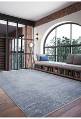 A modern room with large arched windows, a cushioned bench with storage, a tripod floor lamp, brick walls, and the Contemporary Serenity - Machine-Washable Rug JR1884—ideal for high-traffic areas—on a wooden floor.