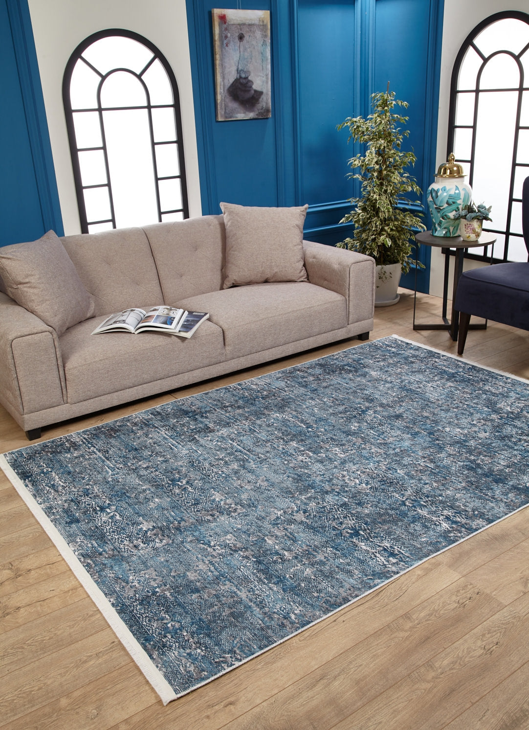 A modern living room with a beige sofa, open magazine, Contemporary Serenity - Machine-Washable Rug JR1884 (Custom Size) ideal for high-traffic areas, black side table with decor, potted plant, and blue paneled walls with arched windows and art.